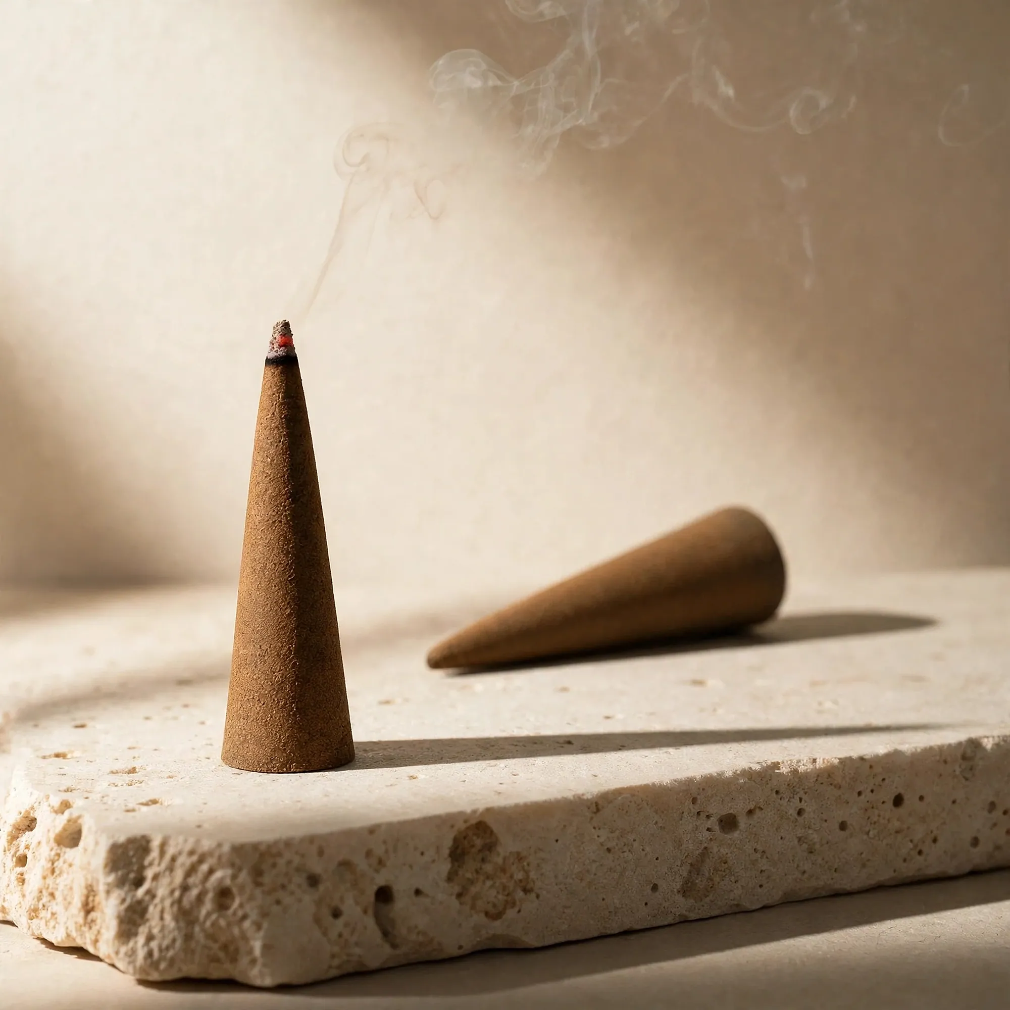A slender incense cone burning on a travertine block, an unlit cone behind it