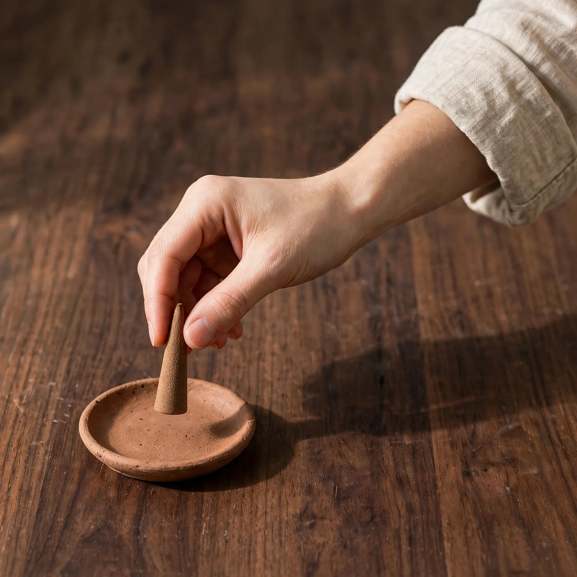 A hand placing an incense cone onto a terracotta dish